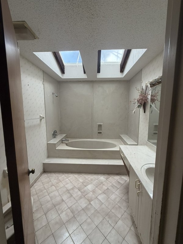 An old master bathroom with a tiled step-up tub and pink floor tile in a Palm Coast flip
